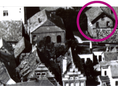 Luftaufnahme, im Vordergrund ein Giebelhaus und Gebäude mit Spitzdach, im Hintergrund ein einstöckiges Gebäude mit mehreren Schornsteinen und großen Bögen, rechts daneben ein zweistöckiges Gebäude mit runder Markierung.
