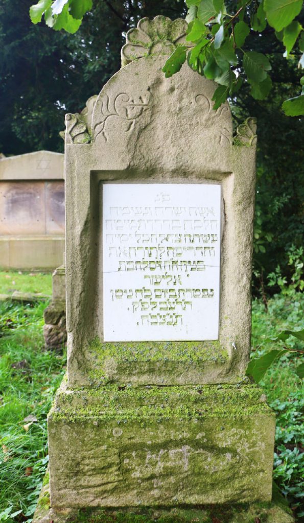Hoher Grabstein aus hellem Stein, eine Platte in der Mitte eingelassen aus hellem Stein mit eingemeißelter hebräischer Schrift.