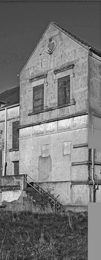 Black-and-white photograph of a two-storey building; the door is bricked up, and the windows are boarded up.