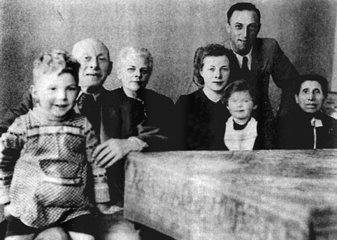 Seven people sitting/standing at a table, including two children.
