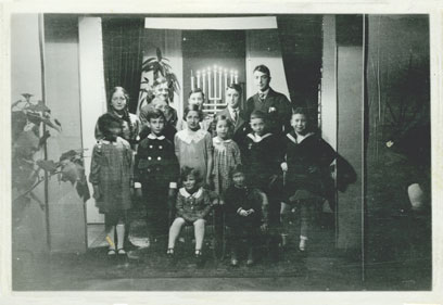 Photograph of 14 children in front of a window with Hanukkah burning.